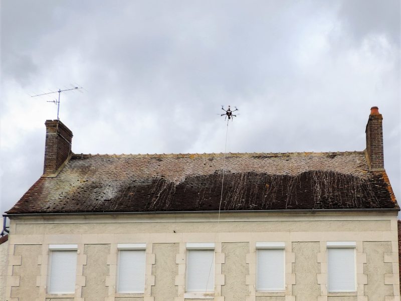 Drone Aries Atlas équipé d'un système de nettoyage haute pression en train de nettoyer une toiture de maison - Prestations Nettoyage Drone Reims